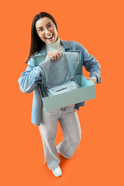 Γυναικείος πωλητής με τζιν σε κουτί σε πορτοκαλί φόντο - Φωτογραφία, εικόνα