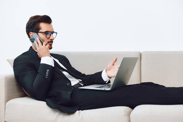Sofa férfi kanapé hívás felnőtt üzletember telefon munka bézs íróasztal győztes életmód videó laptop portré intelligens irodai beszélgetés üzleti telefon fiatal mosoly - Fotó, kép