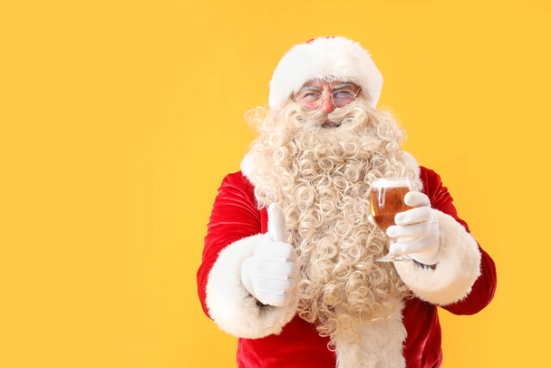 Père Noël avec verre de bière montrant pouce vers le haut sur fond jaune - Photo, image
