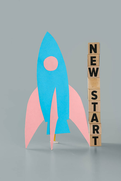 Кубики з текстом NEW START і паперовою ракетою на сірому фоні - Фото, зображення