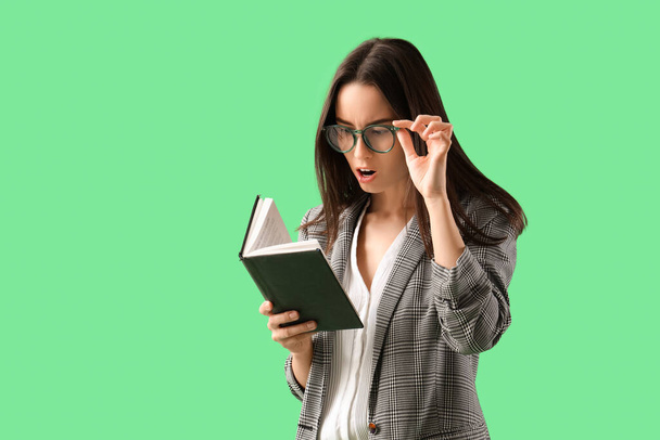 Šokovaný mladý businesswoman v brýlích čtení knihy na zeleném pozadí - Fotografie, Obrázek