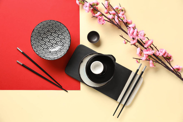 Bowls with cups, chopsticks and sakura branch on color background. Chinese table setting - Photo, Image