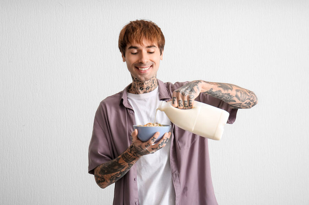 Mann gießt Milch in Schüssel mit Müsliringen auf weißem Hintergrund - Foto, Bild