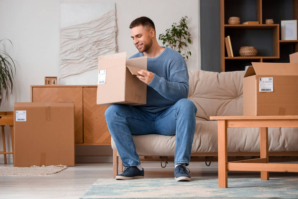 Молодий чоловік розпаковує посилку на дивані вдома - Фото, зображення