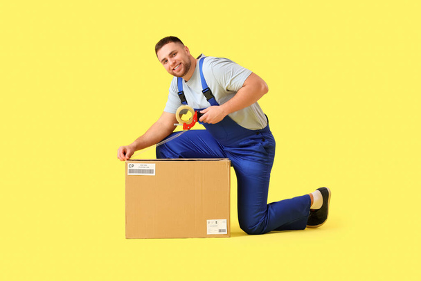 黄色の背景のテープが付いている男性の急使のパッキング小包箱 - 写真・画像