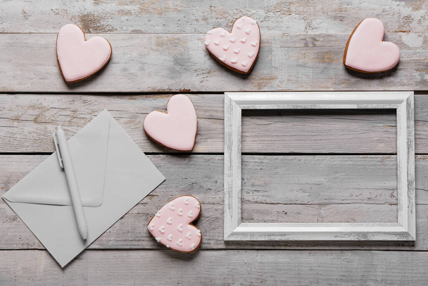 Ízletes szív alakú sütik képkerettel, borítékkal és tollal szürke fa háttéren. Valentin-napi ünneplés - Fotó, kép