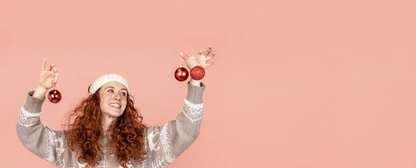 cheerful christmas young woman in christmas sweater and santa hat holding christmas decoration. Merry Christmas and happy new year concept - Photo, Image