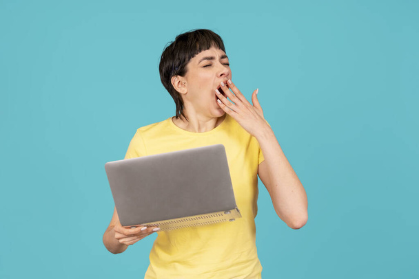 黄色いTシャツを着た女性は,ラップトップ,青い背景のPCコンピュータを使用しています. ワークスタディ,バーチャルトレーニング,eラーニング,オンライン教育ウェビナーのコンセプトを見る - 写真・画像