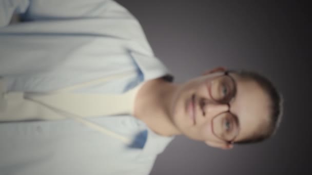 Vertikální střední pomalý portrét mladé bělošky koordinátorky IT, která ukazuje svůj identifikační odznak na kameře stojící na šedém pozadí studia - Záběry, video