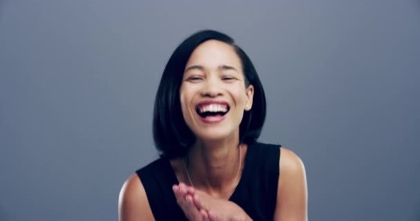 Asian, face and woman laugh in studio with funny joke, happiness or reaction to comedy. Happy, portrait and girl with comic, joy or lol emoji with humor and smile in grey background or mockup. - Footage, Video