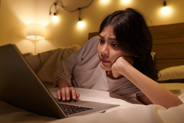Teenagermädchen liest Artikel und Posts in sozialen Medien, wenn sie mit Laptop im Bett liegt - Foto, Bild