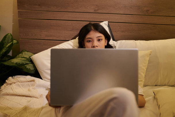 Zmęczona młoda kobieta leżąca w łóżku z otwartym laptopem, czytająca artykuł lub oglądająca wideo - Zdjęcie, obraz
