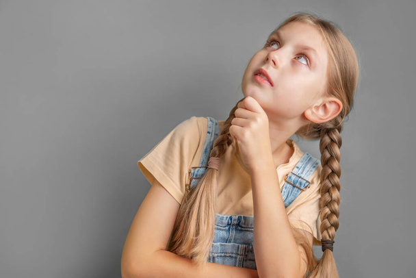 Egy befonott hajú kislány portréja, aki gondolkodik és felnéz - Fotó, kép