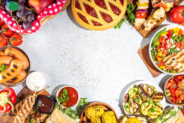Various picnic barbeque food and drink flatlay. Summer bbq picnic food, assorted grilled meats, kebabs, vegetable, fruit salad, traditional picnic summer pie cake, sandwiches, top view copy space - Photo, Image