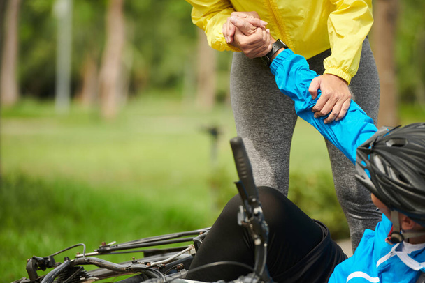 Обрізане зображення жінки, яка допомагає чоловікові впасти з велосипеда, щоб піднятися - Фото, зображення