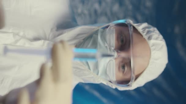 Вертикальная грудь до замедленной съемки портрет молодой кавказской женщины-врача в защитном покрытии, очках и маске для лица, смотрящей в камеру во время нажатия шприца для удаления воздуха - Кадры, видео