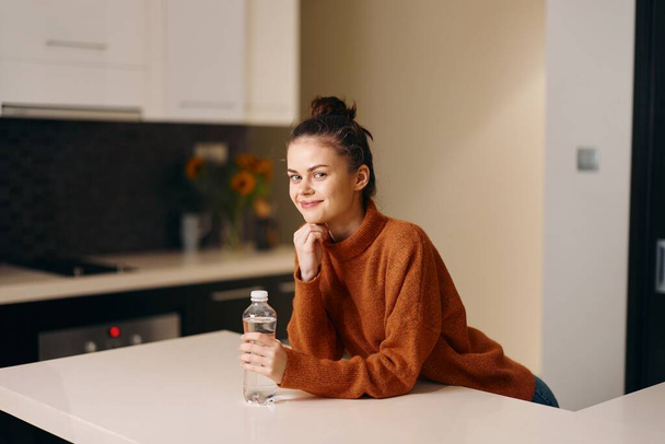 Estilo de vida saludable: Joven hembra sosteniendo una botella de agua, sentada en casa - Foto, imagen