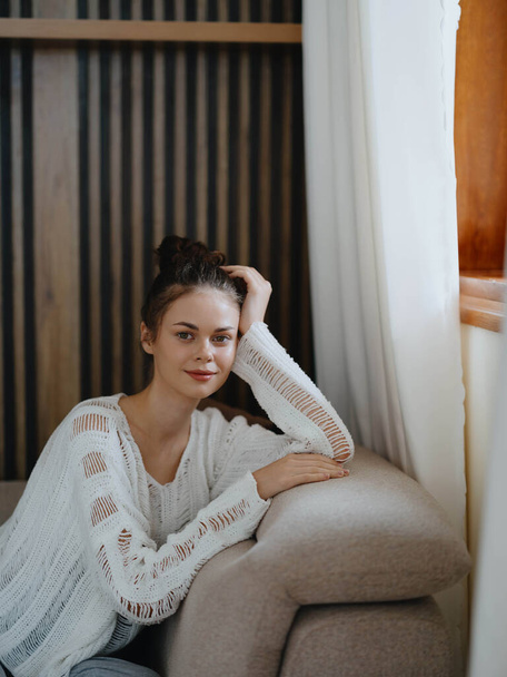 Woman in sweater and home pants relaxing lying on the couch at home, cozy day off in comfort, real lifestyle with a smile. High quality photo - Photo, Image
