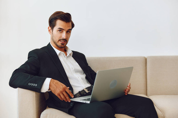 Takım elbiseli adam ofis işadamı görünümlü erkek kanepe oturan beyaz video yaşam tarzı serbest masa bir teknoloji modern dizüstü bilgisayar işi - Fotoğraf, Görsel