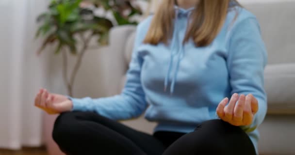 Молода біла жінка практикує йогу та медитацію вдома, сидячи на підлозі у вітальні в позі лотоса. Концепція свідомої медитації та благополуччя. Високоякісні 4k кадри - Кадри, відео