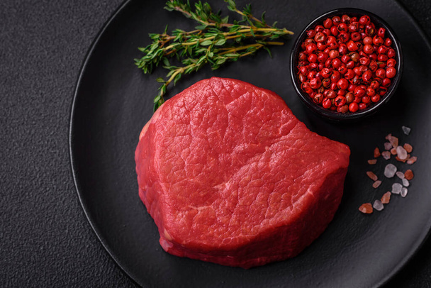 Fresh juicy raw filet mignon with salt, spices and herbs on a dark textured background - Photo, Image