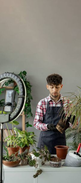 Blogueur masculin replantant des plantes d'intérieur à la maison enregistrement en direct diffusé pour les réseaux sociaux faisant son passe-temps préféré à la maison. Bannière verticale. Espace de copie - Photo, image