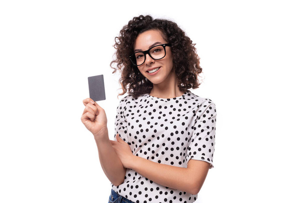 Puantiyeli bluz giymiş kıvırcık saçlı beyaz bir iş kadını kredi kartı tutuyor.. - Fotoğraf, Görsel