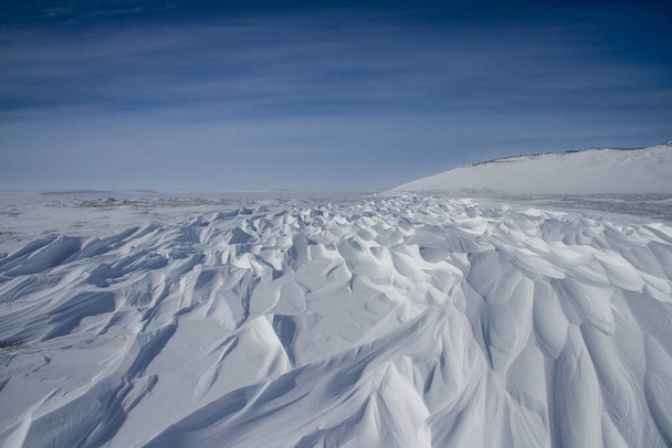 Kauniita sastrugi-kuvioita, tuulen aiheuttamia aaltomaisia harjuja kovan lumen pinnalla, pehmeät pilvet taivaalla, lähellä Arviat Nunavut Kanadaa - Valokuva, kuva