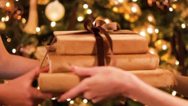 Крупним планом жіночі руки дарують і отримують різдвяні подарунки на тлі прикрашеної ялинки. Дама в стильній вечірній сукні, що представляє купу книг, пов'язаних стрічкою зі своїм найкращим другом. - Кадри, відео