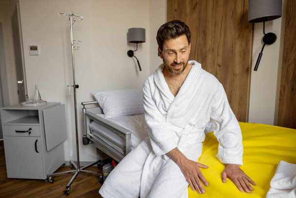 L'uomo controlla il materasso prima di coricarsi nel reparto medico. Concetto di soggiorno confortevole in suite mediche - Foto, immagini