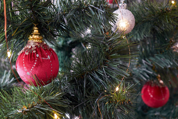 As bolas de Natal estão penduradas na árvore. Luzes de guirlanda estão queimando perto deles. - Foto, Imagem