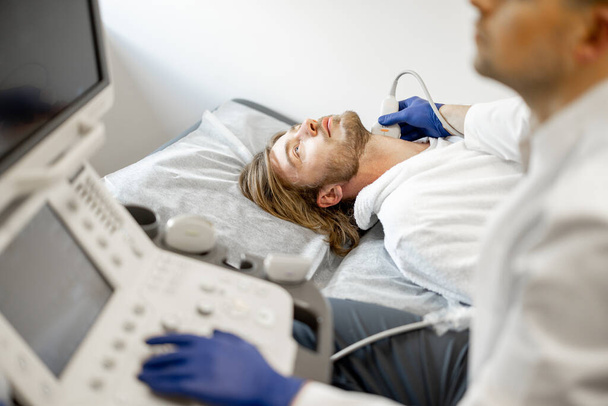 Junger Mann während einer Ultraschalluntersuchung der Halsschlagader. Konzept der Ultraschalldiagnostik und Männergesundheit. Idee der Untersuchung von Herz-Kreislauf-Erkrankungen - Foto, Bild
