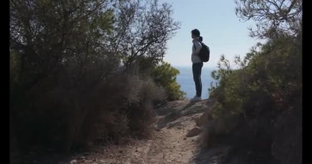 Жінка середнього віку з рюкзаком, що стоїть на скелястому узбережжі і насолоджується видом на Середземне море. Сольні подорожі, відпустка, подорож, активний спосіб життя. - Кадри, відео