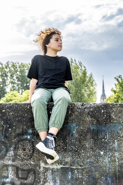 Девушка сидит на бетонной стене, за ней голубое небо - Фото, изображение