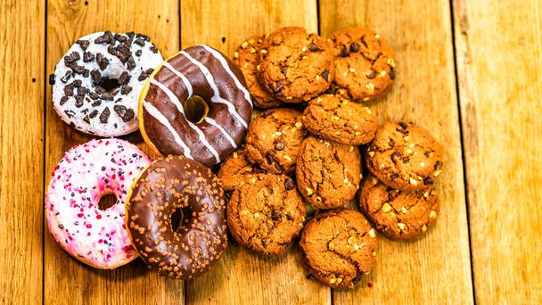Colorful donuts and biscuits on wooden table. Sweet icing sugar food with glazed sprinkles, doughnut with chocolate frosting. Top view with copy space - Photo, Image