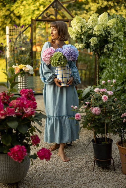 Portrait of a young woman in dress standing with beautiful bouquet in vase in garden. Floristry and gardening concept - Valokuva, kuva
