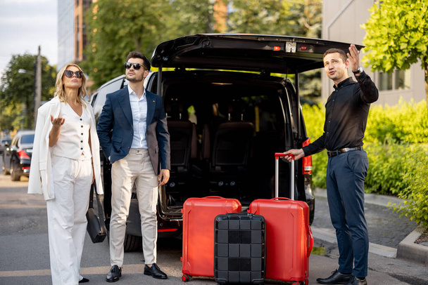 Liikemiespariskunta seisoo tila-auton taksilla odottamassa kuljettajaa tai kantajaa auttamaan heitä matkalaukkujen kanssa. Työmatkojen ja matkojen käsite - Valokuva, kuva