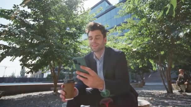 Elegante imprenditore surf cellulare internet seduta parco verde alla pausa caffè da vicino. Rilassato uomo d'affari di successo guardando i social media da smartphone sulla strada. Uomo felice navigazione app mobile - Filmati, video