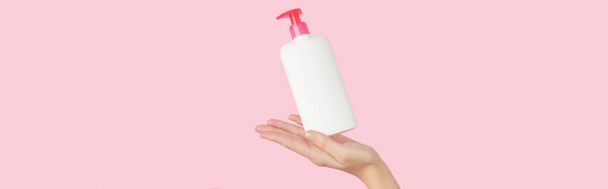 Жінки рука тримає білу пляшку на пастельному рожевому фоні. Концепція догляду за красою. - Фото, зображення