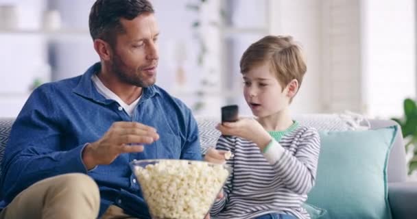 Rodzina, popcorn i mężczyzna oglądający telewizję z synem na kanapie w salonie. Miłość, uśmiech lub szczęście z ojcem i dzieckiem streaming filmu, filmu lub wideo w mieszkaniu. - Materiał filmowy, wideo