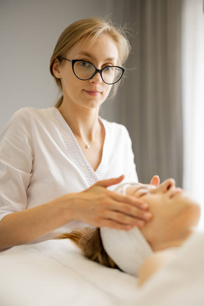 Esteticista faz massagem facial profissional para o rosto das mulheres no salão de beleza. Conceito de cuidado facial - Foto, Imagem