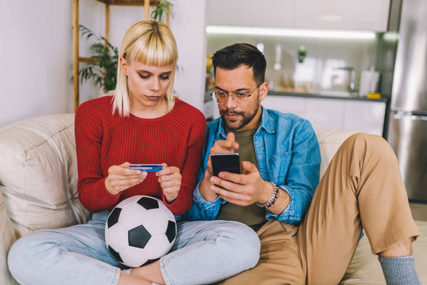 Junges Paar verfolgt Fußballspiel auf digitalem Tablet und nutzt Kreditkarte für Online-Wetten. - Foto, Bild