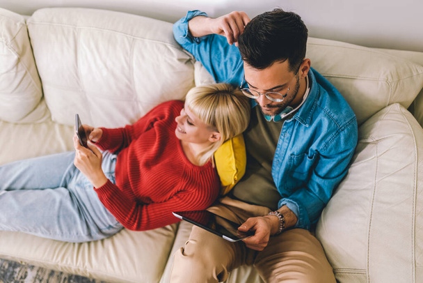 Bonito casal abraçando relaxante no sofá e usando tablet digital e telefone. - Foto, Imagem