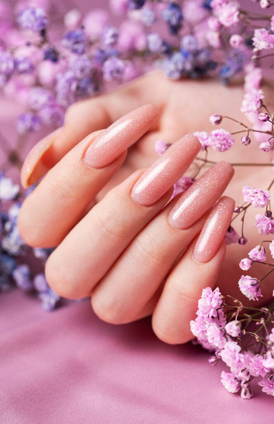 Kobiece ręce z różowym projektu paznokci trzymać cyganów kwiaty. Różowy paznokci polski manicure na różowym tle - Zdjęcie, obraz