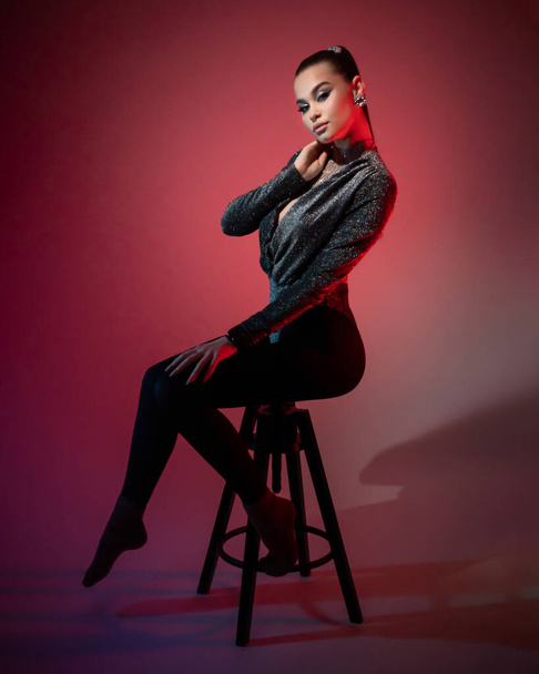 赤いランタンの光の下でスタジオの高い椅子に座っている若い美しい女の子ポーズ - 写真・画像