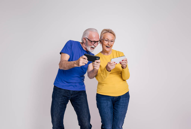 ホワイトバックグラウンドでスマートフォン上でビデオゲームをプレイメガネで興奮成熟した夫と妻 - 写真・画像