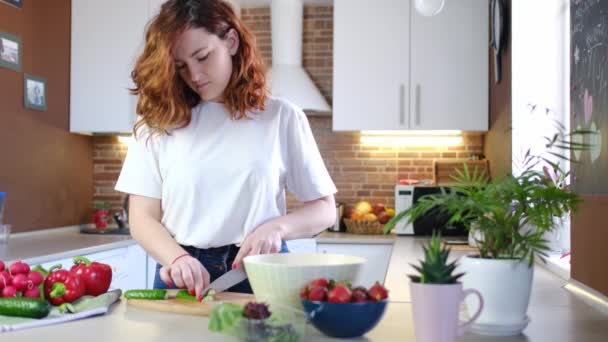 若い白人女性は,野菜や有機成分を閉じたバックグラウンドで家庭のキッチンで健康的な食品サラダを作ります. 健康的な朝食。 ビーガンライフスタイル - 映像、動画