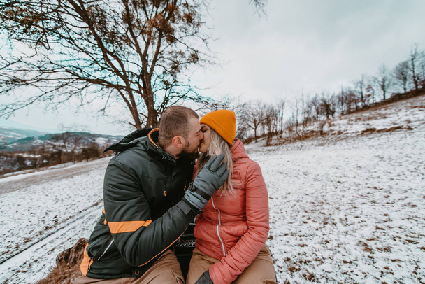  Romantik bir çift, karlı arazide neşeyle bir avluya binerken şefkatli bir kucaklaşmayı ve öpüşmeyi paylaşır. Kış macerasının ortasında büyülü ve tutkulu bir an yaratır..  - Fotoğraf, Görsel