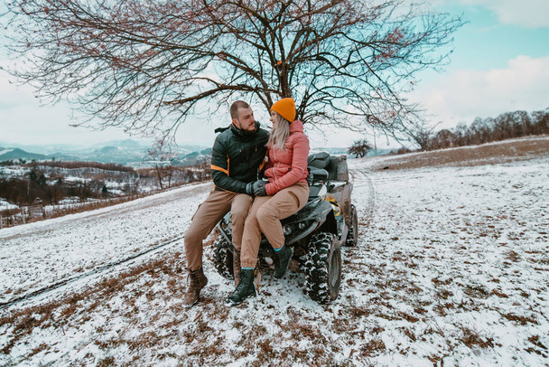  Romantyczna para dzieli czuły uścisk i pocałunki podczas radosnej jazdy quadem po śnieżnym krajobrazie, tworząc magiczny i namiętny moment pośród chłodnej przygody.  - Zdjęcie, obraz