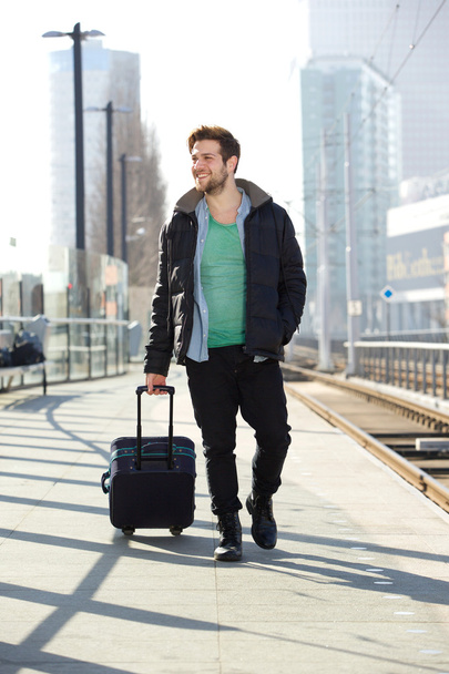 Jeune homme souriant avec valise sur le quai de la gare
 - Photo, image